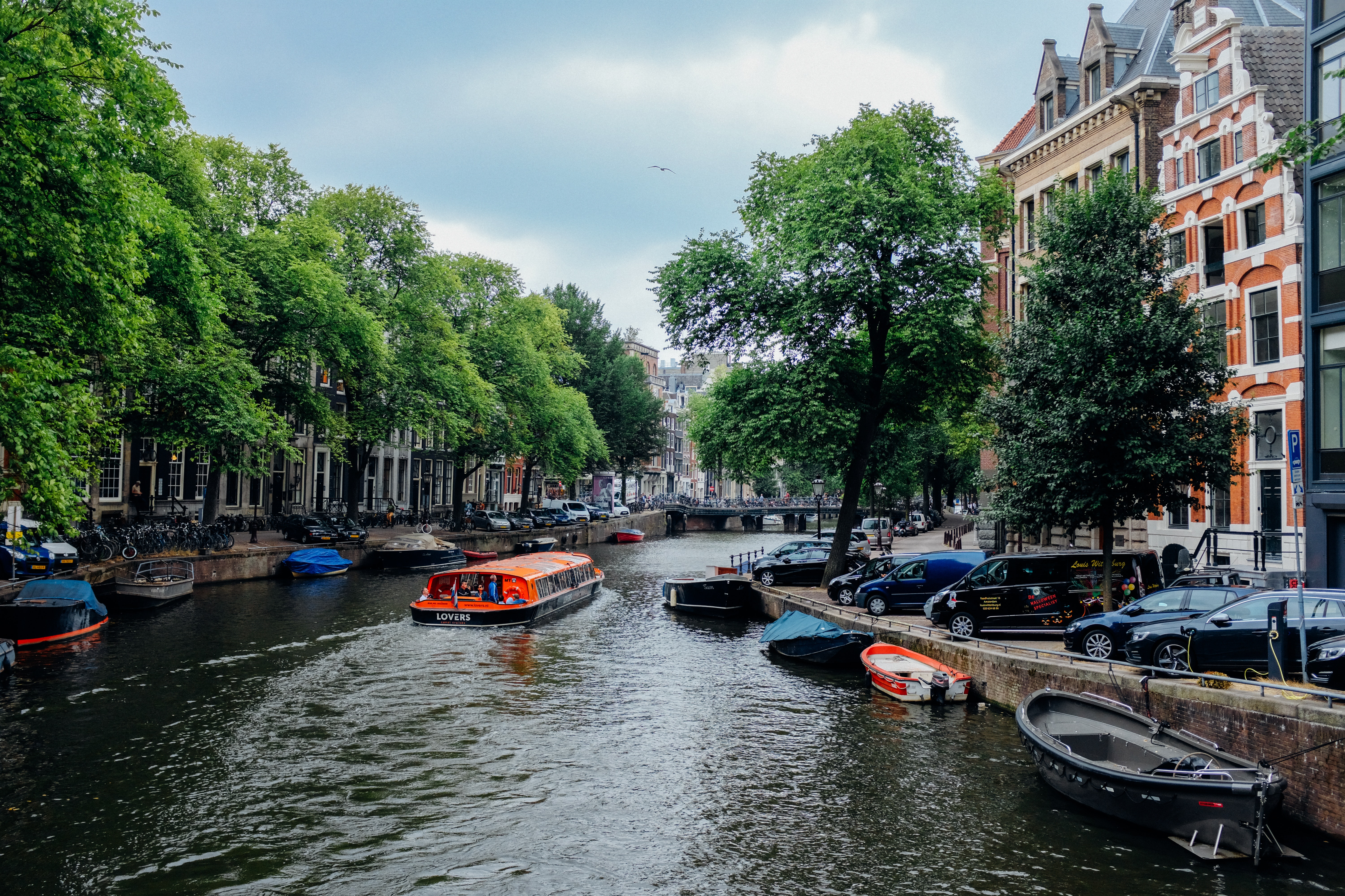 Amsterdam canal with orange boat in the middle and green trees around it